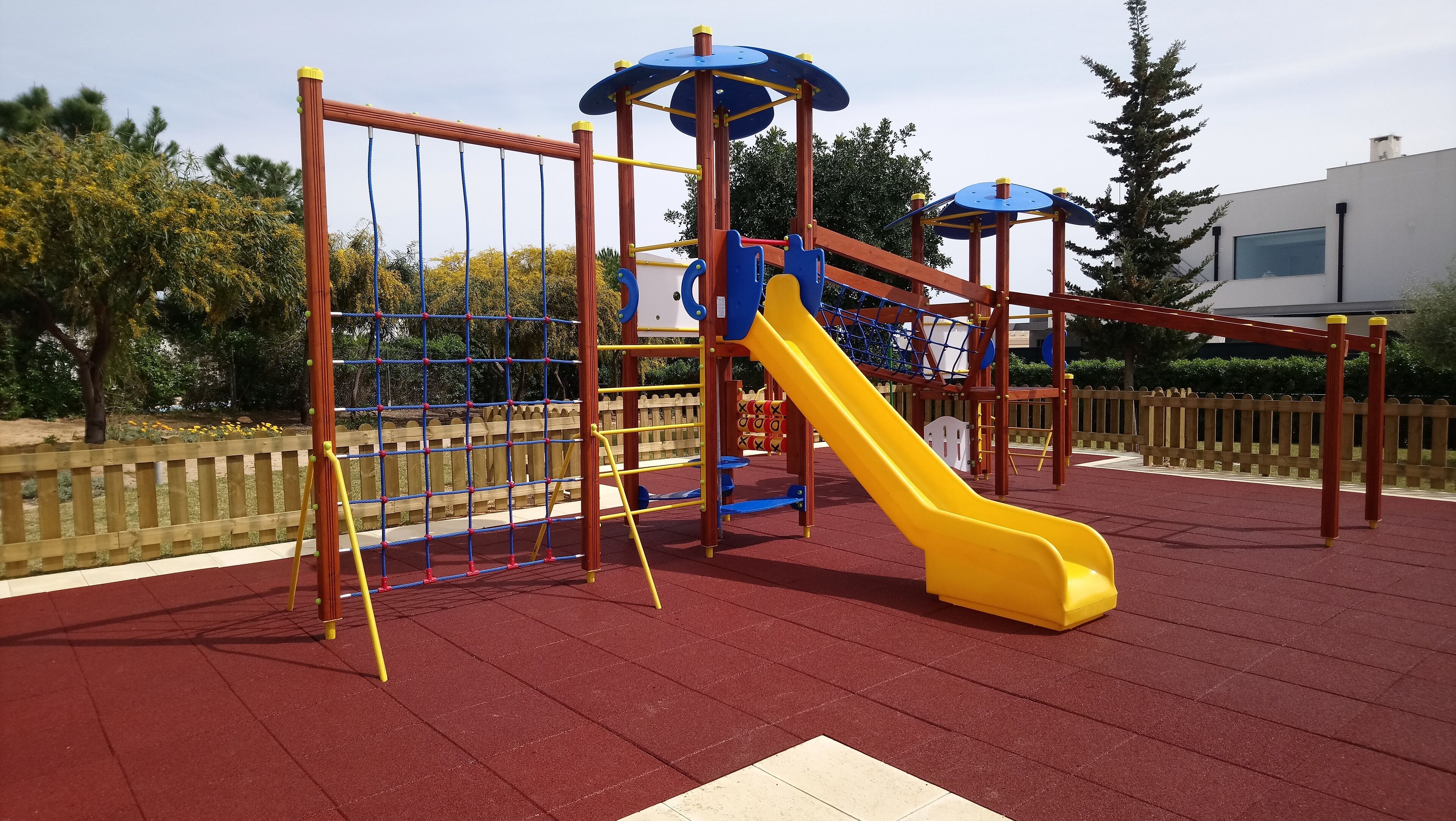 A playground with a yellow slide, climbing structures, and a fenced area.
