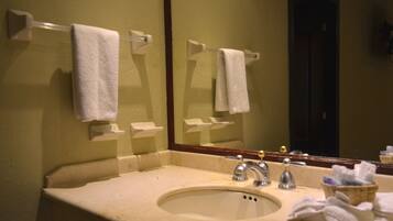 Un bany amb un lavabo, dues barra de tovalloles, un mirall i una cistella plena de tovalloles.