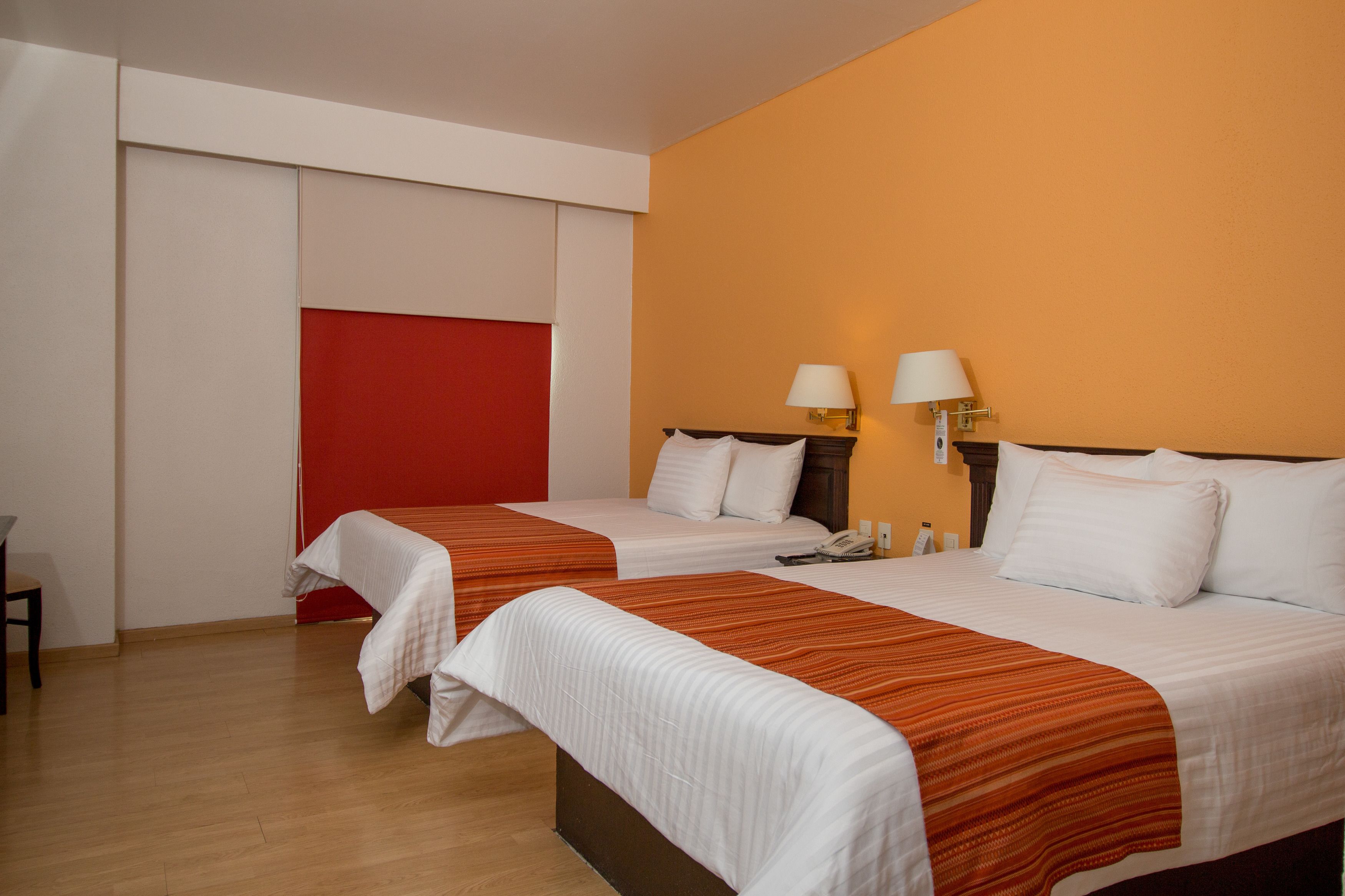 Camera d'albergo con due letti, una parete decorata a rosso e due abat-jour.