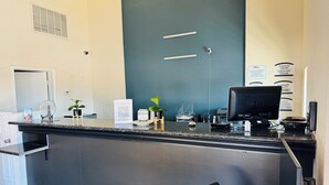 Un comptoir d’accueil d’hôtel avec un ordinateur, un téléphone et une petite plante.