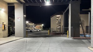 L’entrée d’un parking, avec un sol carrelé, une enseigne indiquant la présence d’un bureau de sécurité, et une zone délimitée par une barrière, avec une piscine visible au fond.