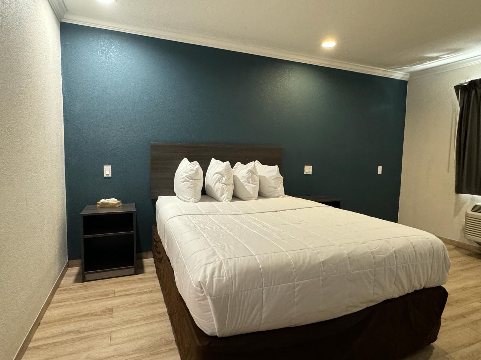 A neatly made bed with white bedding in a room with teal walls and wooden flooring.