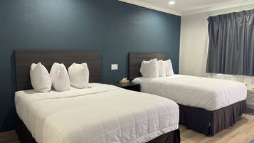 Habitación de hotel con dos camas, cabeceros de madera oscura, ropa de cama blanca y una pared de acento azul.