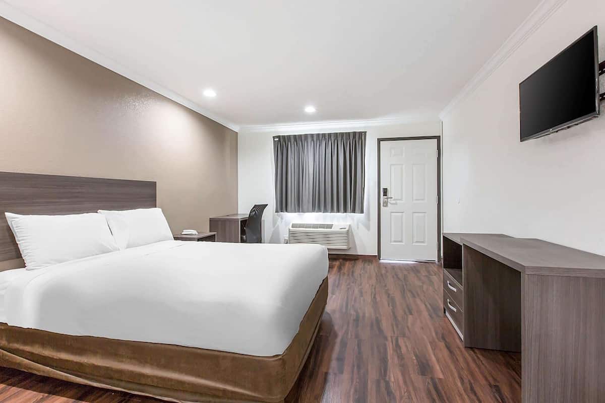Une chambre d’hôtel avec un grand lit, un bureau, une chaise, un téléviseur à écran plat et une porte.