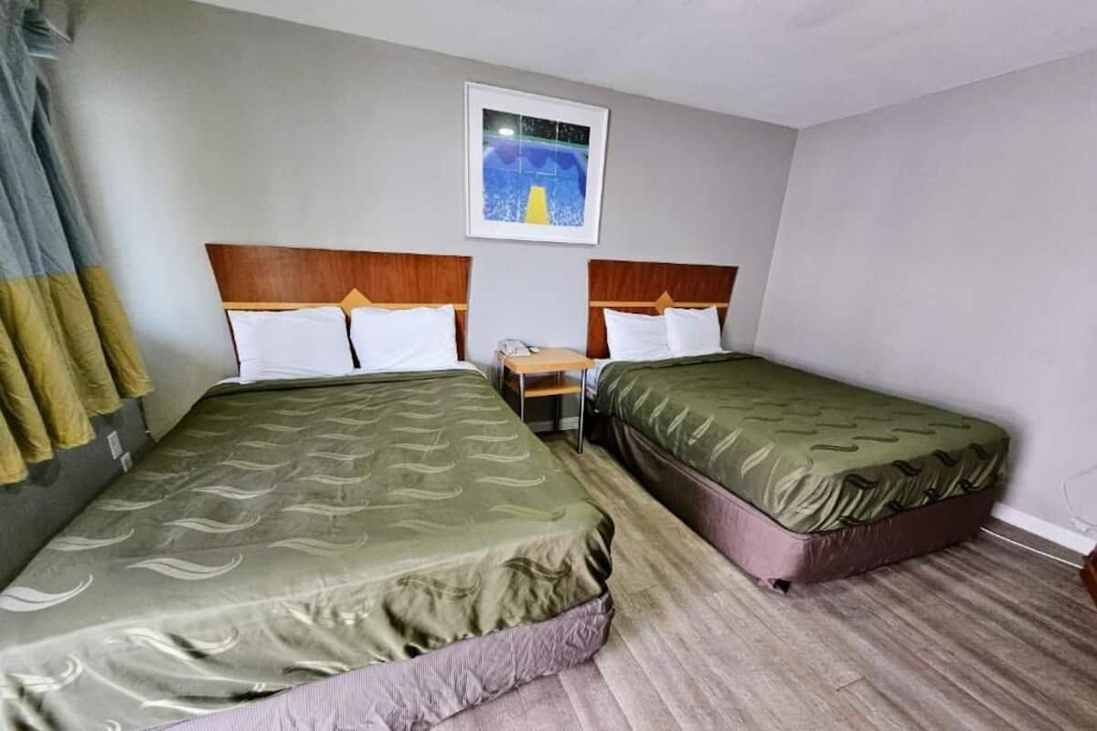 A hotel room with two beds, a small table, and a painting on the wall.