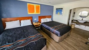 A hotel room with two beds, a wooden headboard, a nightstand, a round mirror, and a small window.