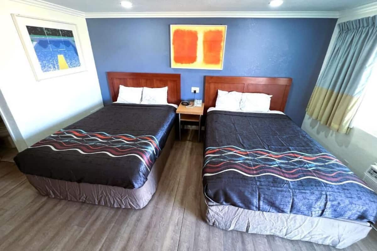 A hotel room with two beds, wooden headboards, and a blue wall with an abstract painting.