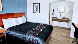 A hotel room with a bed, a bedside table, a chair, a sink, and a mirror.