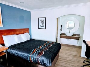 A hotel room with a bed, a bedside table, a chair, a sink, and a mirror.