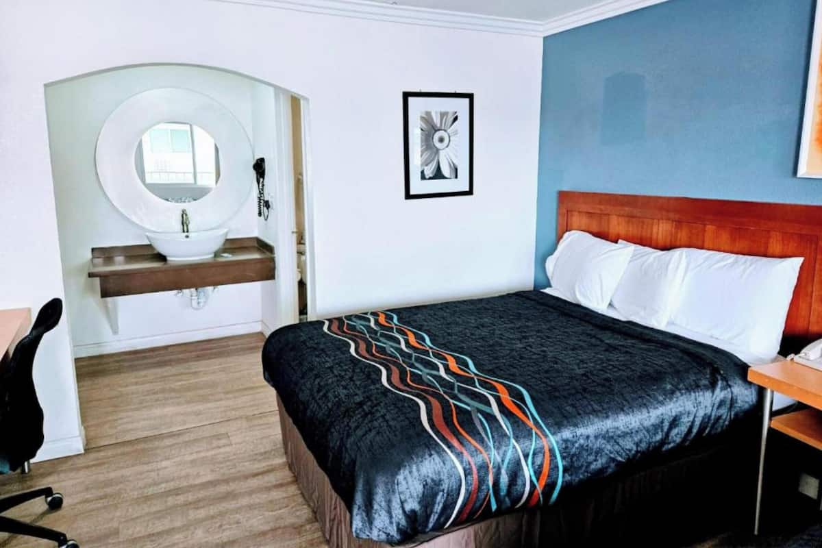 A hotel room with a bed, a wooden headboard, a bedside table, a mirror, and a sink.