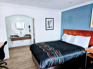 Ett hotellrum med en säng, en sänggavel i trä, en rund spegel, ett handfat och en inramad tavla på väggen.