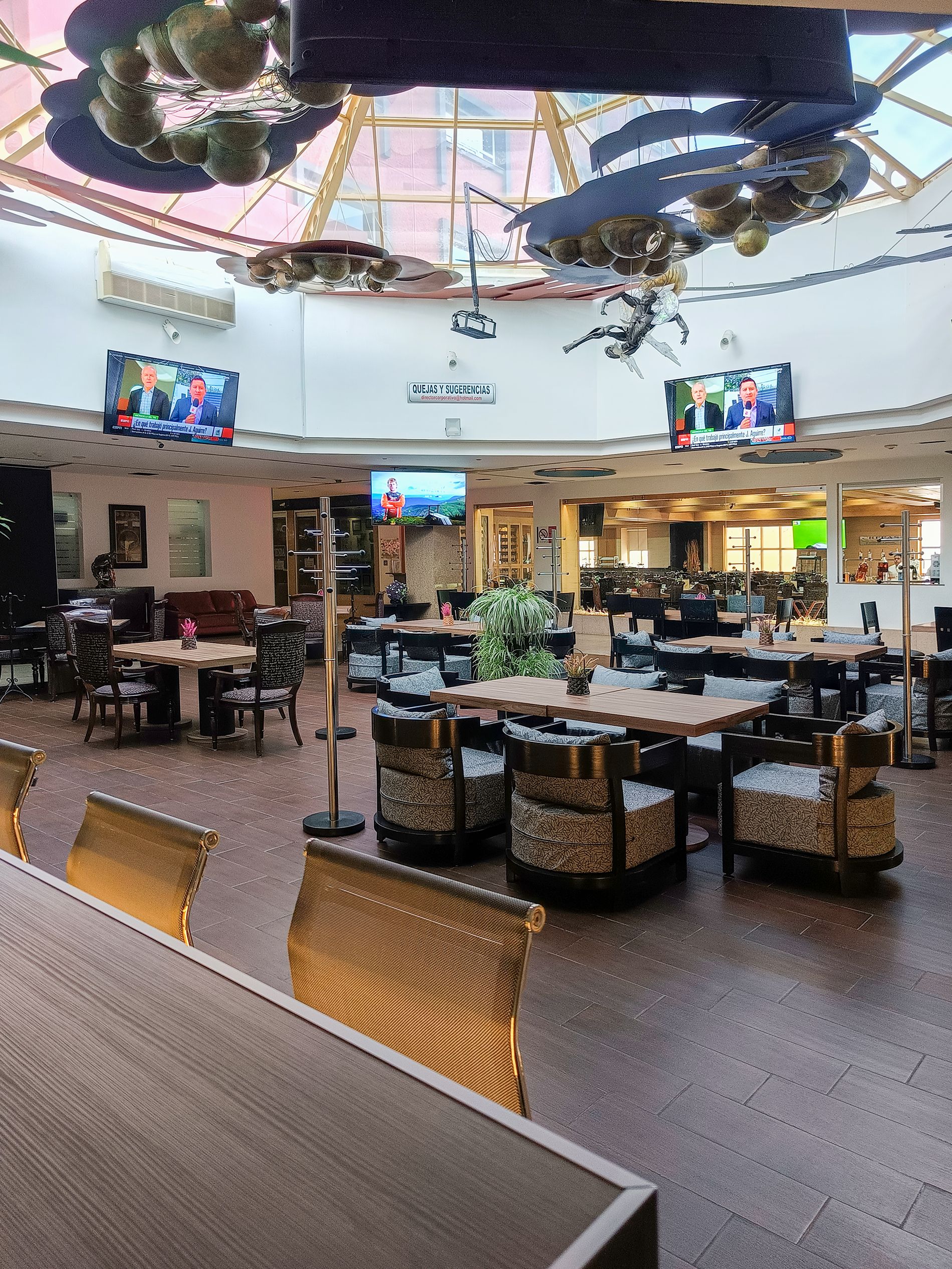 A spacious indoor area with multiple seating arrangements, including tables and chairs, and a large open space with a high ceiling and a glass structure.