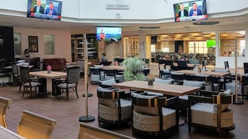 A spacious indoor area with multiple seating arrangements, including tables and chairs, and a large open space with a high ceiling and a glass structure.