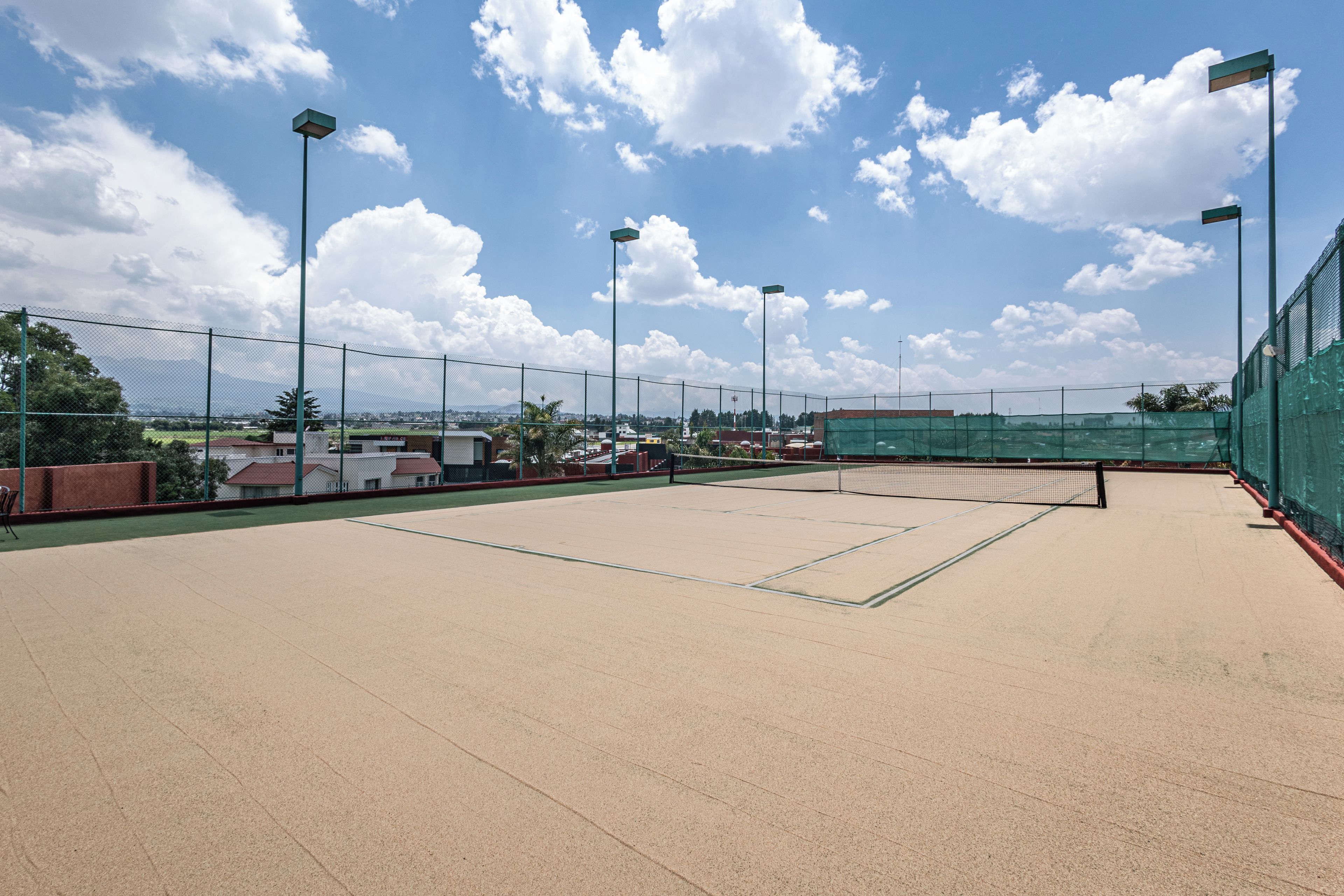 An outdoor tennis court with a net, surrounded by a fence, and under clear skies.