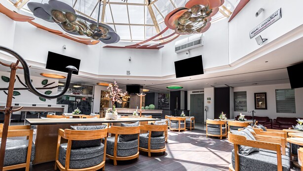 A spacious indoor area with wooden furniture, a central bar area, and a high ceiling with unique lighting fixtures. - Suites Inn La Muralla Metepec (Toluca)