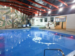 An indoor swimming pool with a mosaic wall, lounge chairs, and a sign indicating supervision requirements. - Suites Inn La Muralla Metepec (Toluca)