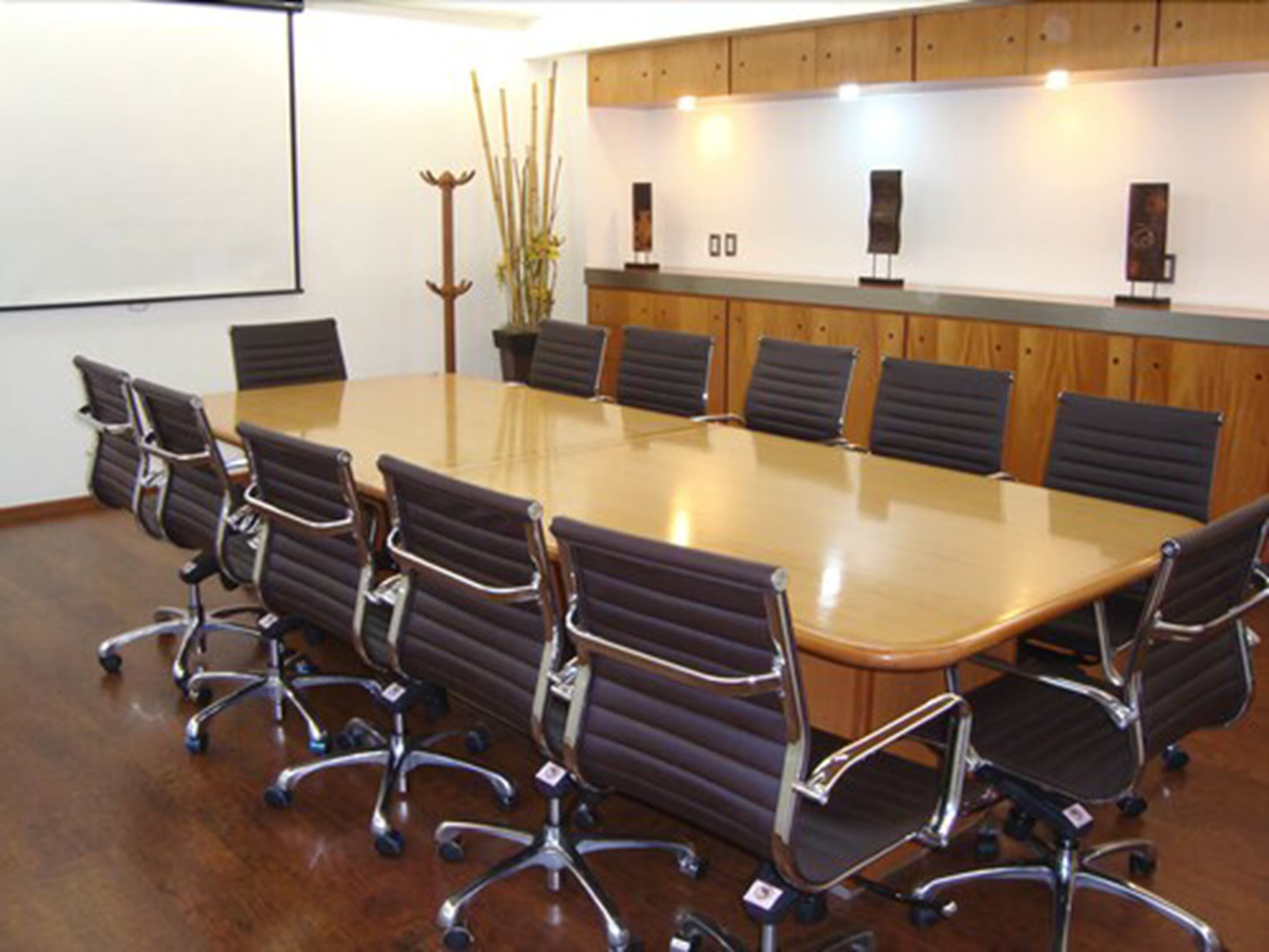 Un salón de conferencias con una larga mesa y seis sillas, paneles de madera en las paredes y una pantalla para proyector.
