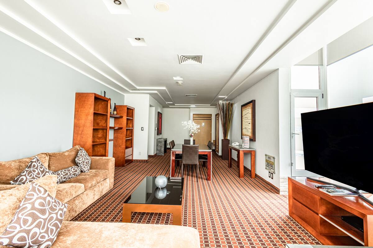 Ett modernt hotellrum med en soffa, TV och en matplats med bord och stolar.