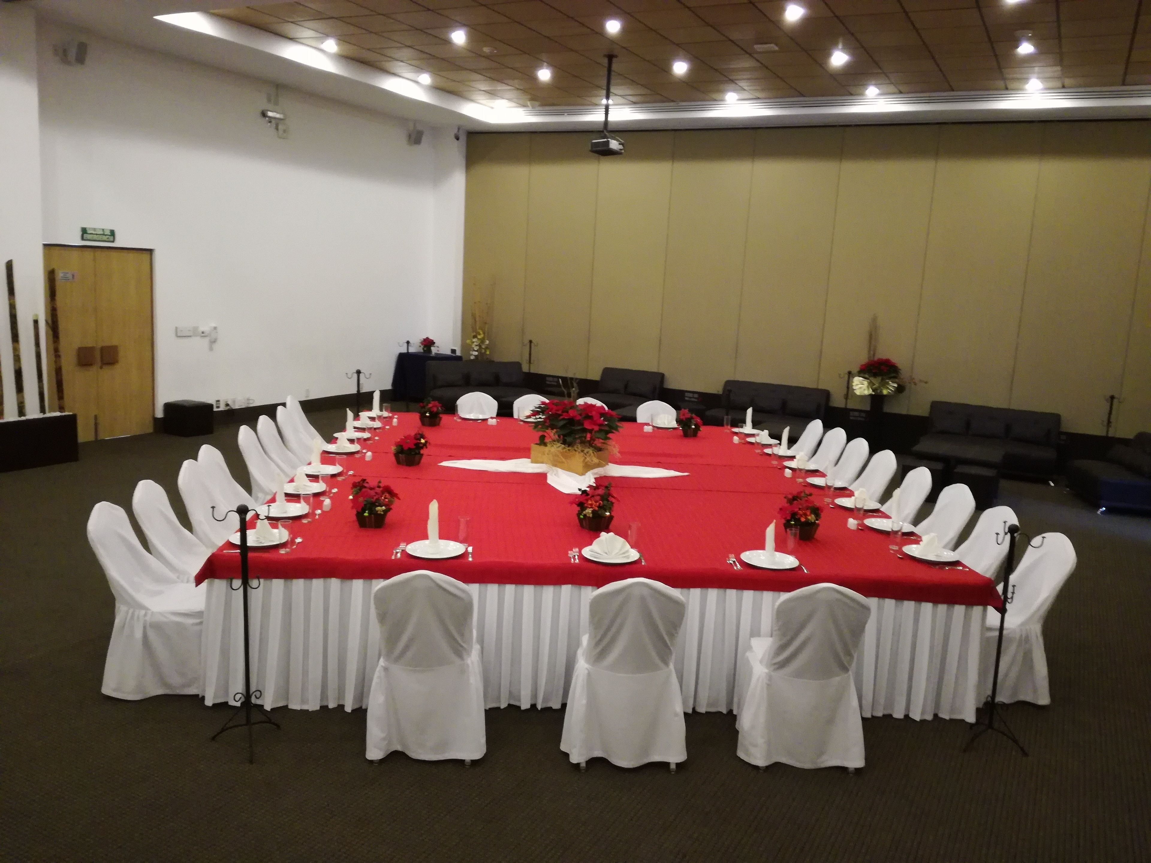 Una sala de conferencias con una mesa roja, sillas blancas y una pantalla de proyector.