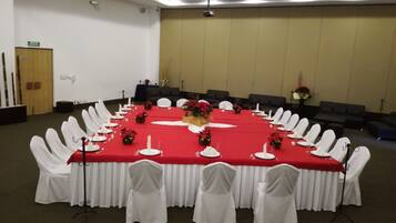 Una sala de conferencias con una mesa roja, sillas blancas y una pantalla de proyector.