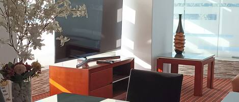 A modern living room with a glass dining table, a flat-screen TV, and a decorative vase.