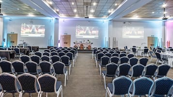 A conference room with rows of chairs facing a stage, equipped with a projector and screen.