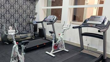 A gym with treadmills, stationary bikes, and a television displaying a news broadcast.