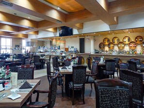 Interior de restaurante con varias mesas y sillas, una zona de bar con botellas y un mural grande en la pared.