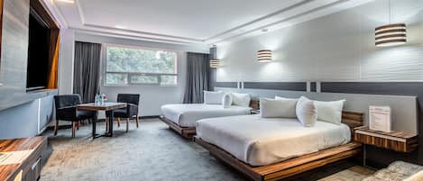 A modern hotel room with two beds, a dining table, and a TV.