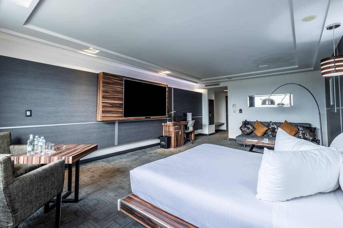 Ett modernt hotellrum med en stor säng, ett skrivbord med en stol, en platt-TV som är monterad på väggen och en soffa med kuddar.