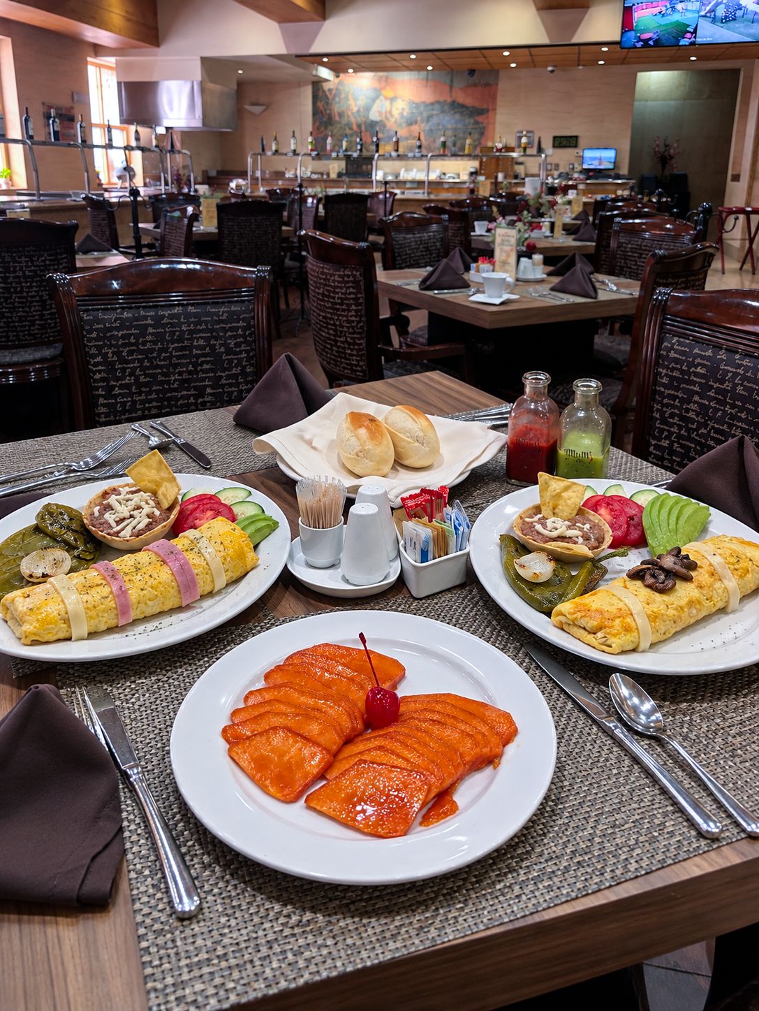 Une salle à manger de restaurant avec des tables dressées pour le service, comprenant des assiettes de nourriture et des condiments.