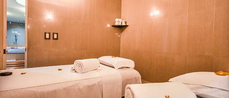 A hotel room with two beds, each with neatly folded towels and a small shelf above.