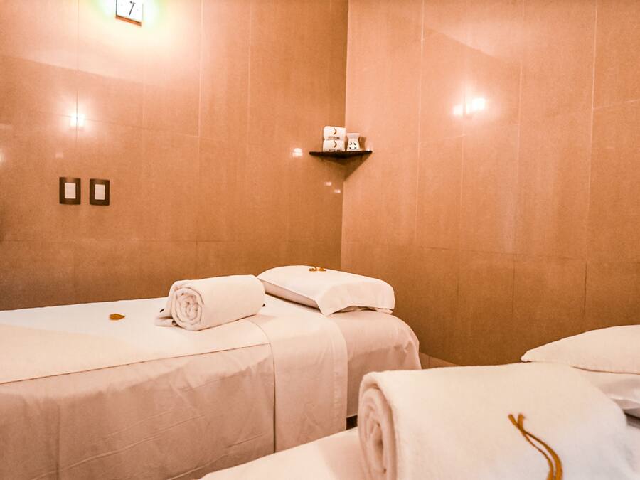 Habitación de hotel con dos camas, cada una con toallas ordenadamente dobladas y un pequeño estante superior.
