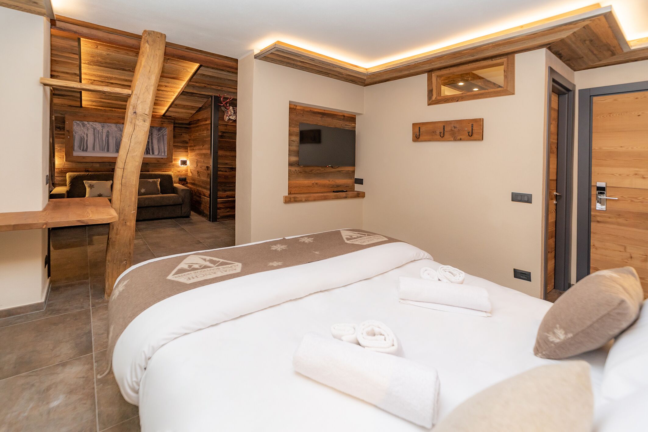 A modern hotel room with a large bed, a wooden desk, and a cozy seating area.
