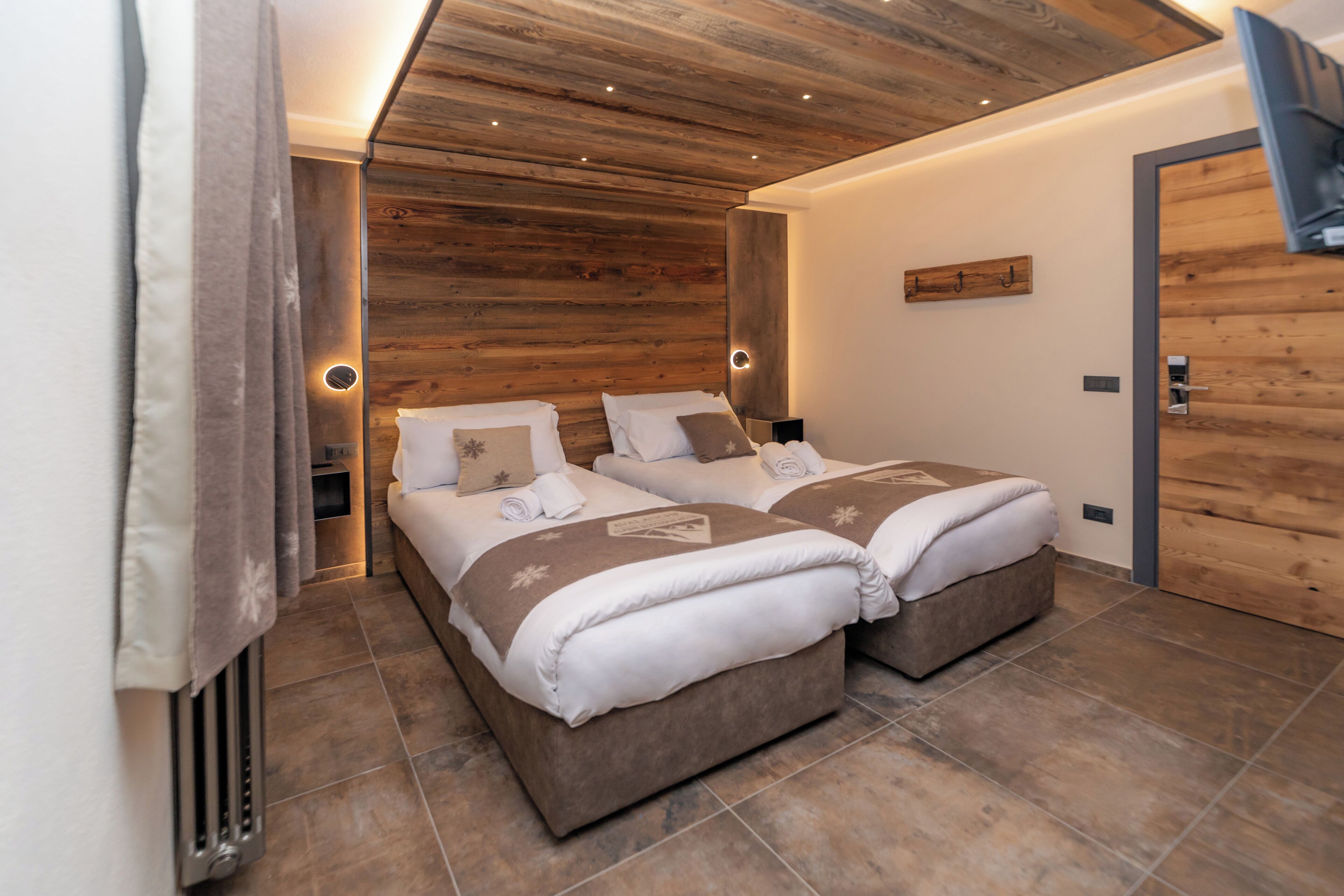 Ein modernes Schlafzimmer mit zwei Betten, Holzvertäfelung an den Wänden und einem an der Wand montierten Flachbildfernseher.