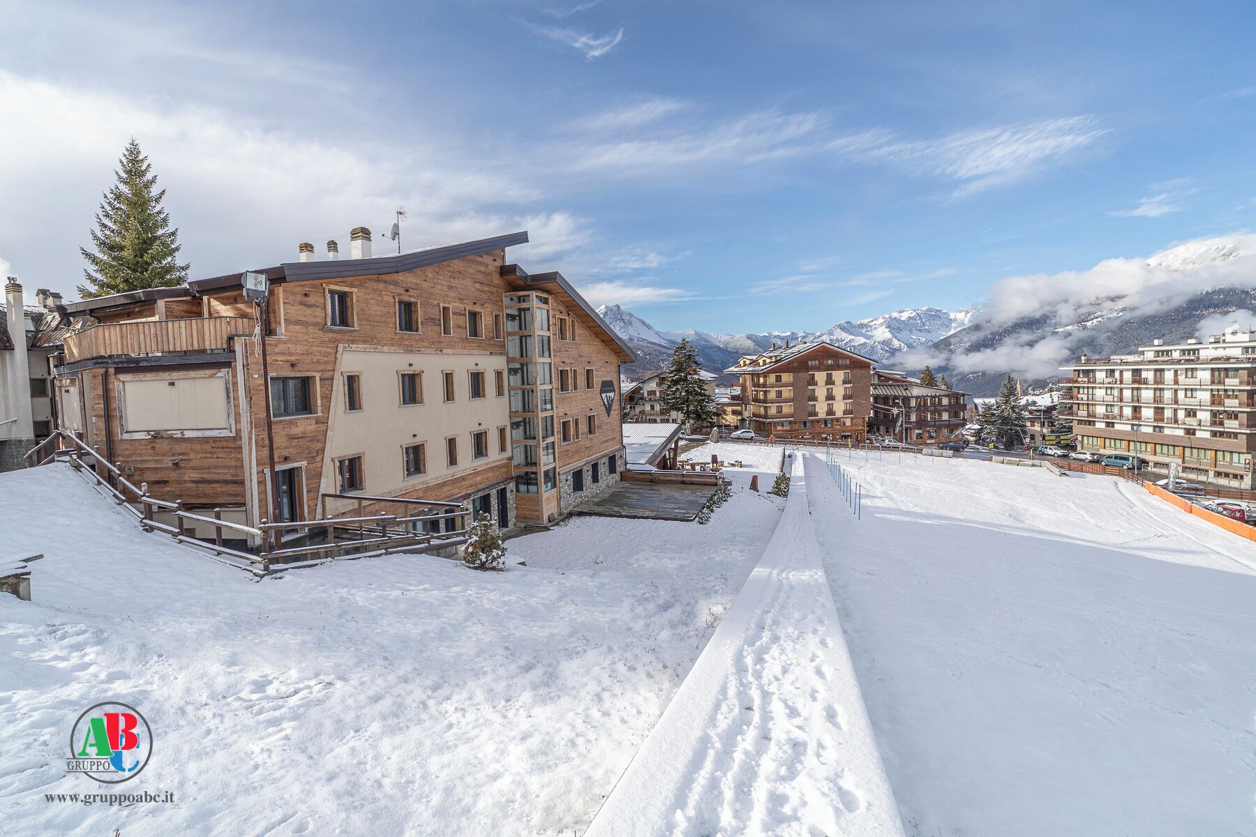 A snow-covered ski resort with multi-story buildings, ski lifts, and a mountainous backdrop.