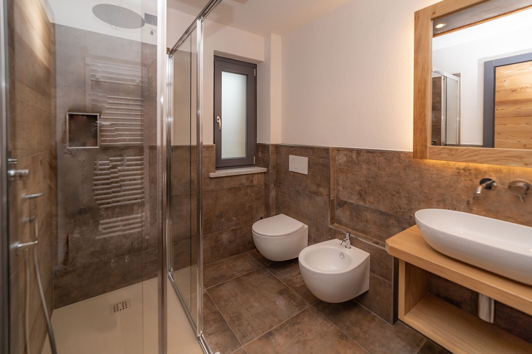 Un bagno moderno con box doccia in vetro, un bidet, un lavabo e uno specchio.
