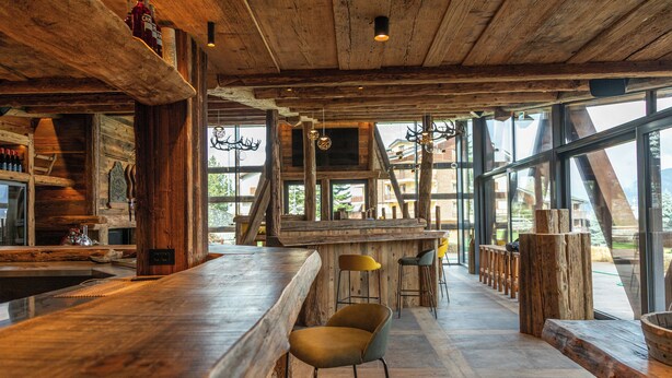 Un interior rústico con barra de madera, asientos y ventanas amplias que ofrecen vistas al exterior.