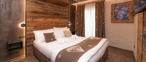 Un dormitorio moderno con cabecera de madera, cama grande con ropa de cama blanca, manta marrón y un cuadro en la pared.