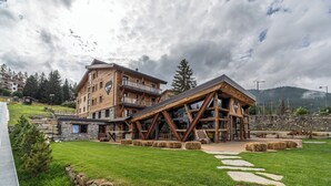 Una cabaña moderna de madera con techo inclinado y varios balcones, con montañas y un cielo nublado de fondo.