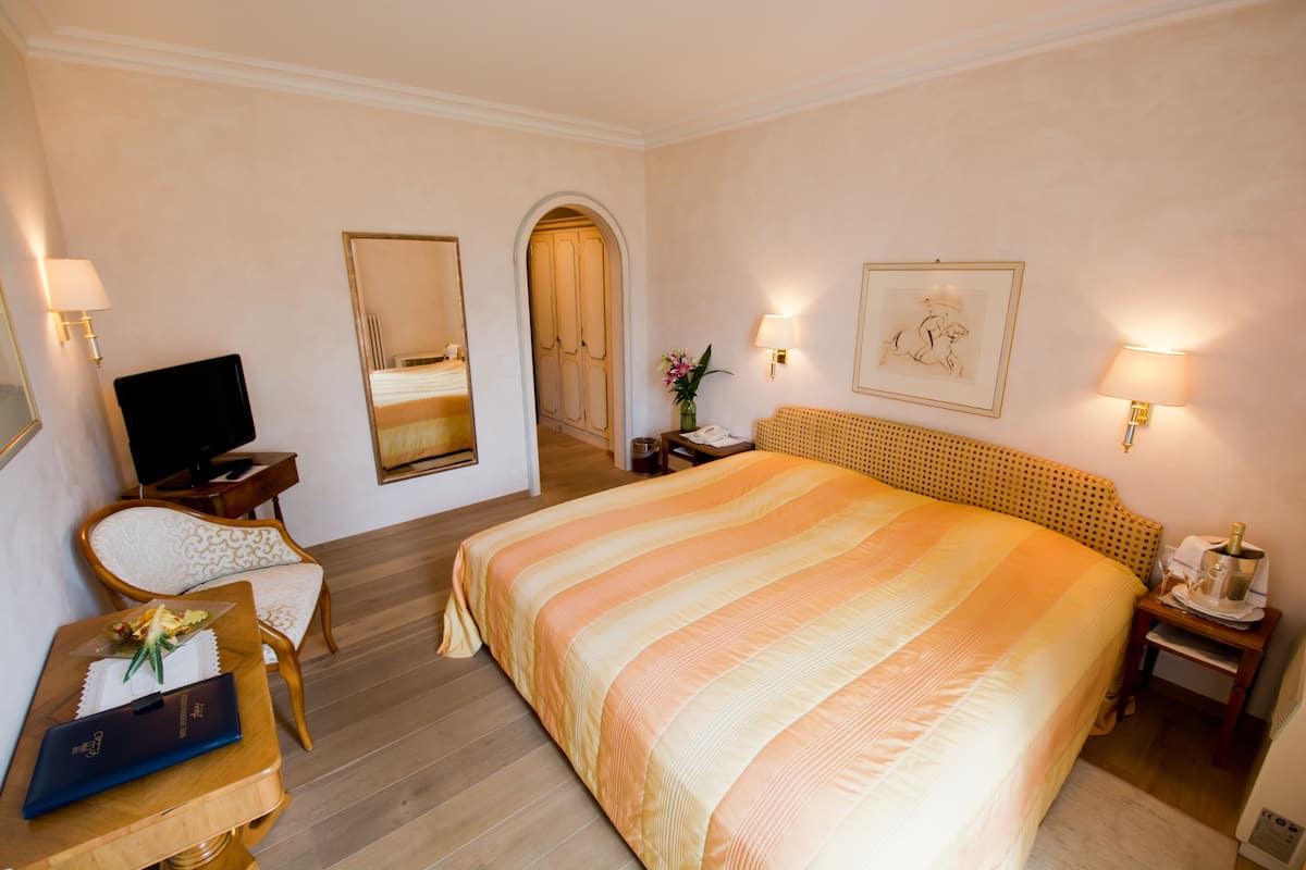 A hotel room with a large bed, a television, a desk with a computer, and a chair.