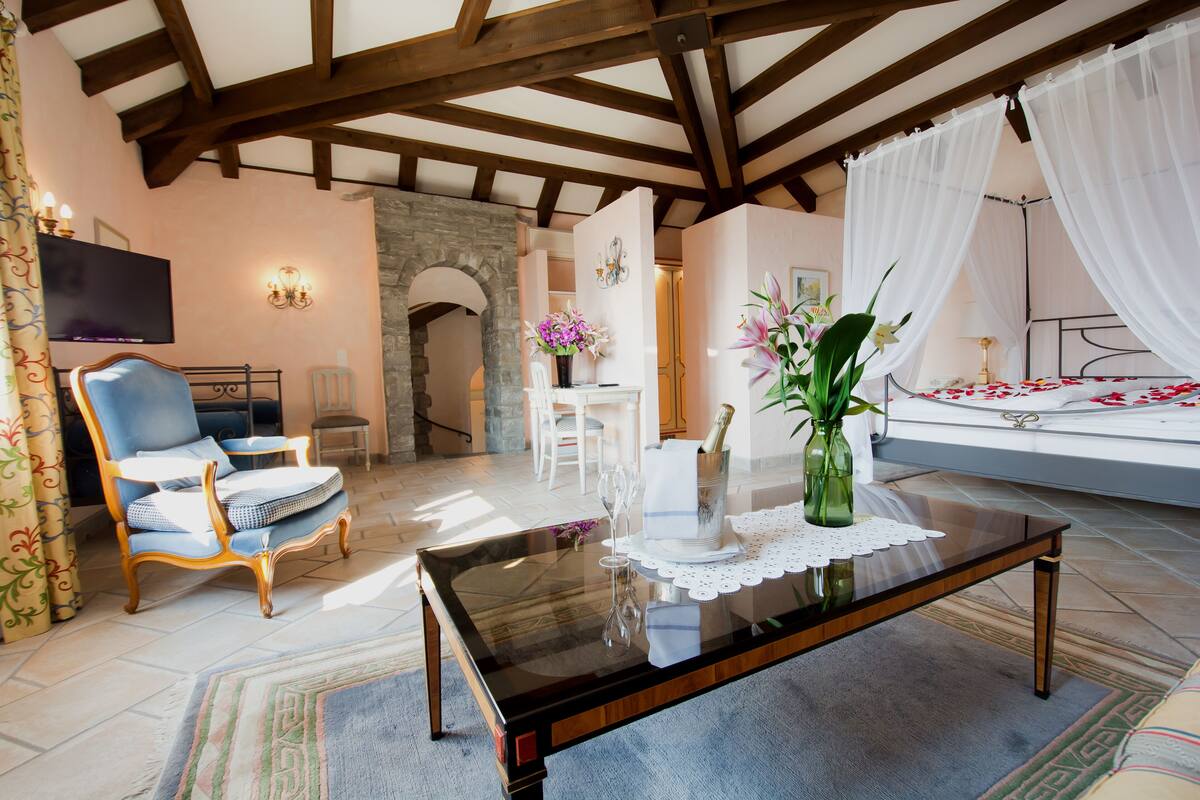 A spacious living room with a high ceiling, a comfortable sofa, a glass coffee table, and a bed with white curtains.