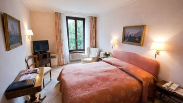 Habitación de hotel con una cama grande, un escritorio con ordenador, una silla, televisión y ventana con cortinas.