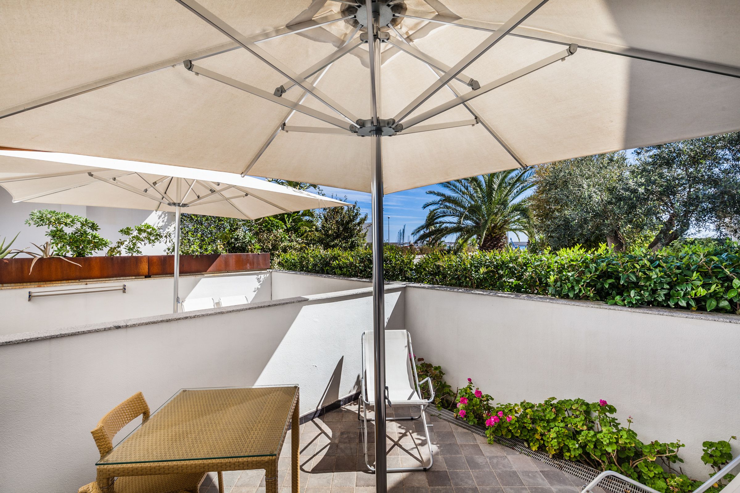 A patio with a table and chairs, a large umbrella, and a view of greenery and trees.