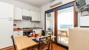 A compact kitchen with white cabinets, a wooden table, and chairs. A large window offers a view of the sea. - Hibiscus Hotel Residence (Siniscola)