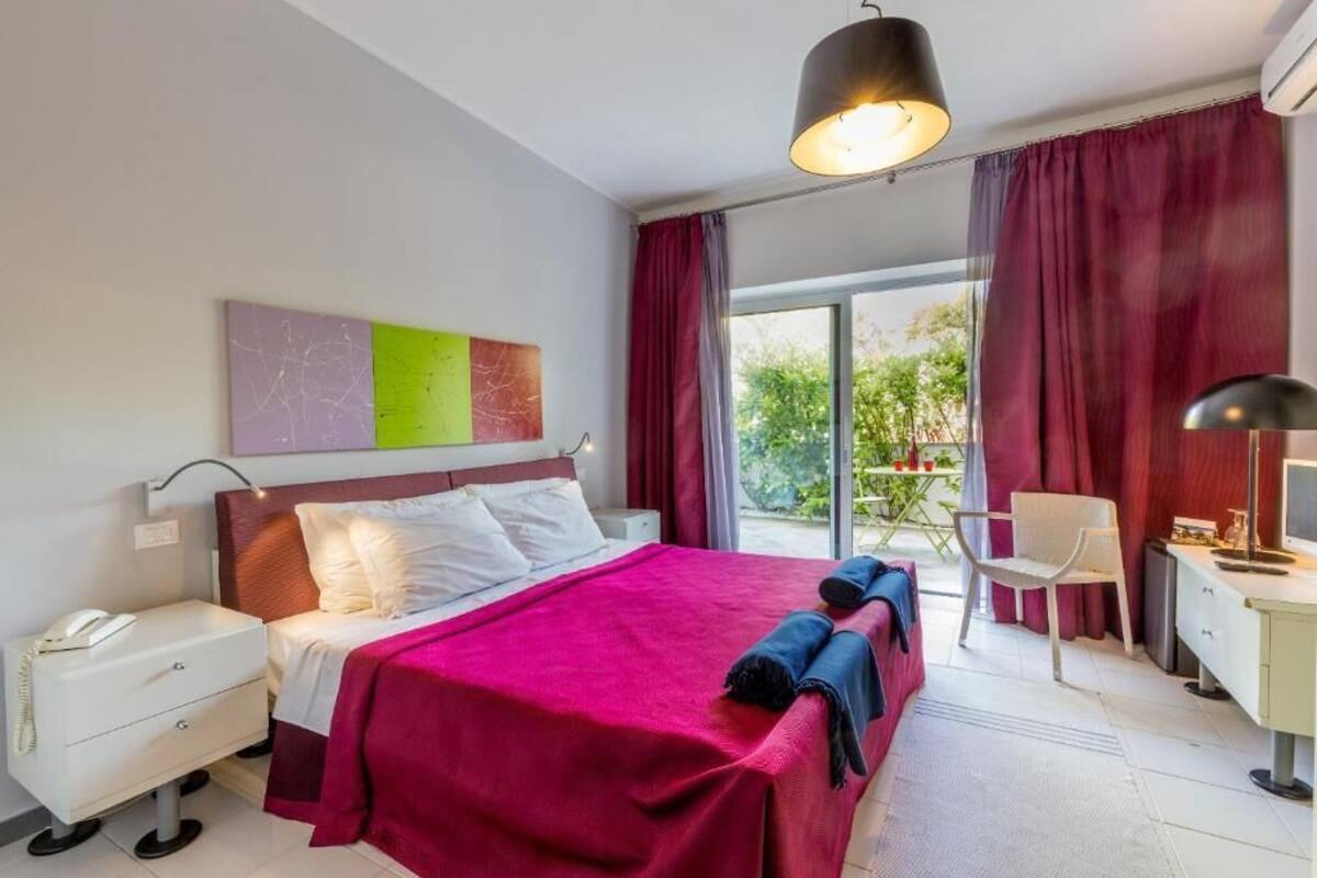 Une chambre d’hôtel moderne dotée d’un grand lit, d’un bureau, d’une chaise et d’un balcon avec une table et des chaises.