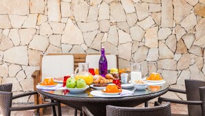 A breakfast table set outdoors with stone walls in the background. - Hibiscus Hotel Residence (Siniscola)