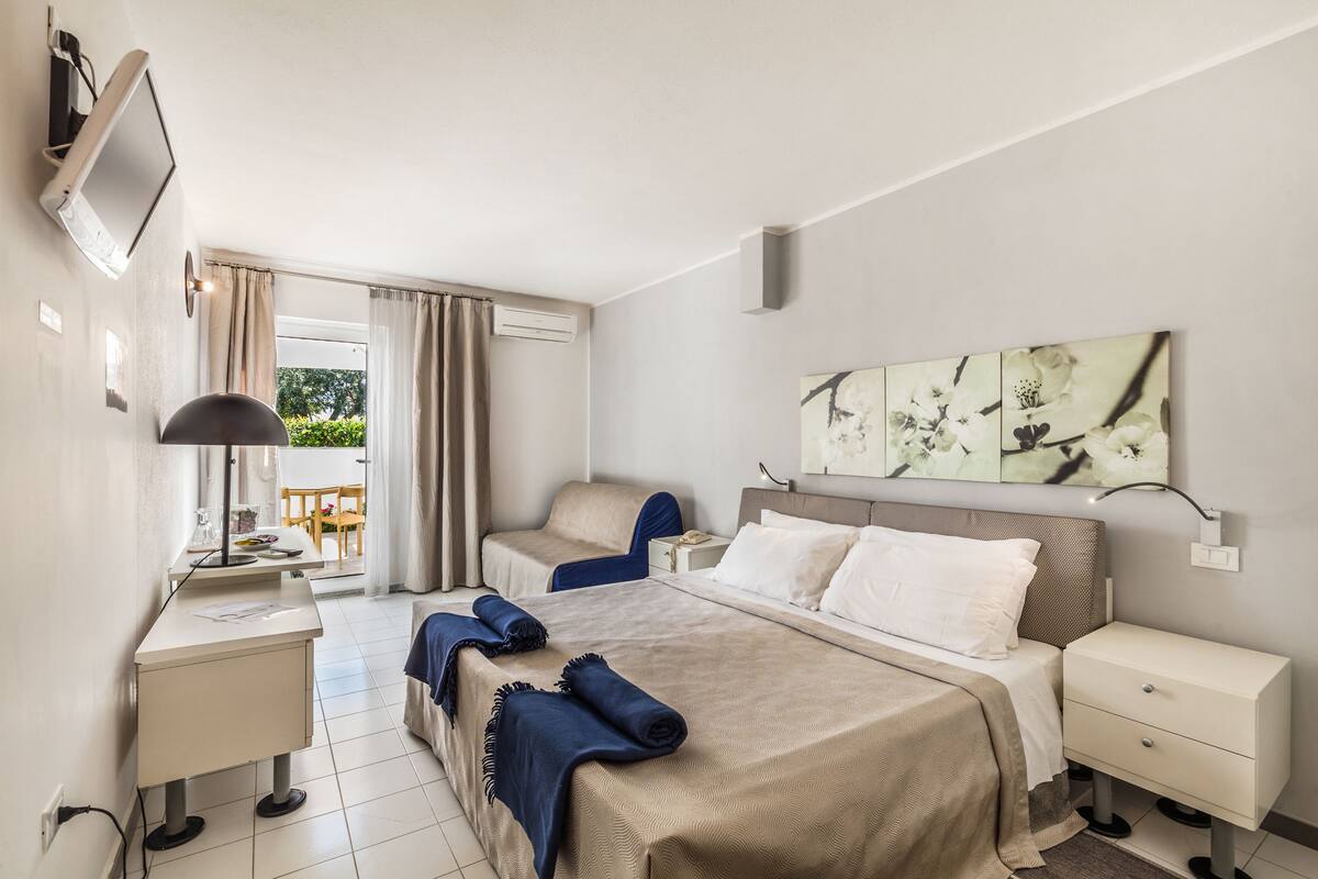 Une chambre d’hôtel comprenant un lit, des tables de chevet, un bureau, une chaise, une télévision et une fenêtre avec des rideaux.