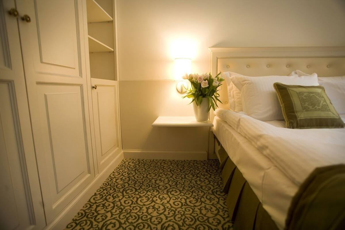Une chambre d’hôtel avec un lit, une table de chevet avec une lampe et des fleurs, et un tapis à motifs.