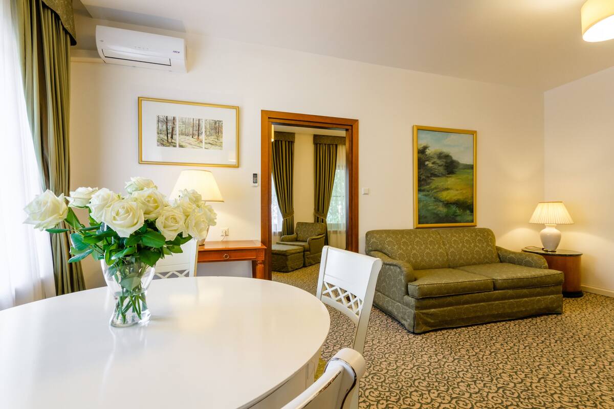 Une chambre d’hôtel avec une table à manger ronde, un canapé, une chaise, une lampe et un tableau au mur.